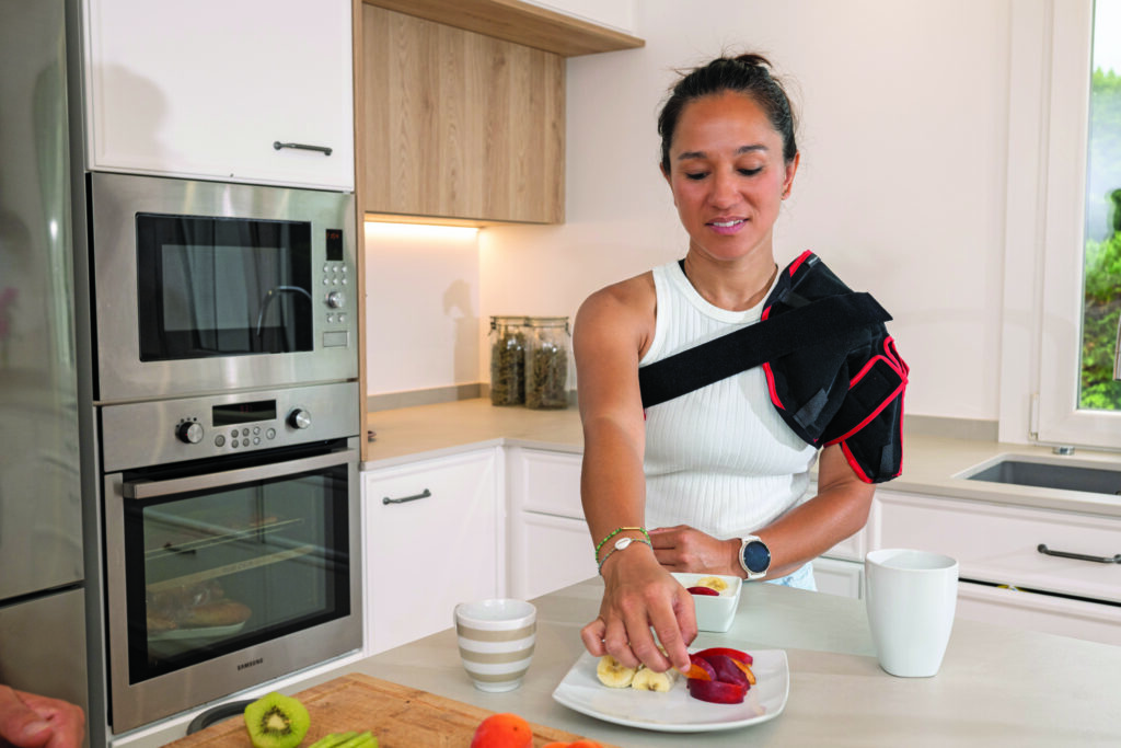 Mujer llevnado la órtesis de crioterapia DonJoy ICE para hombro en la cocina